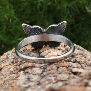 Polished stainless steel butterfly ring with detailed hollow wings on a natural wood base