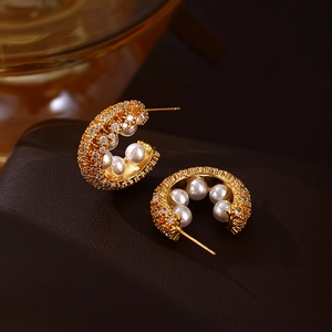 French vintage C-shaped gold earrings with zircon and pearls on elegant brown texture