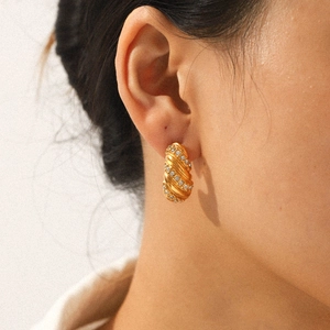 Detail of twisted 18K gold plated hoop earring with zircon inlay on female ear