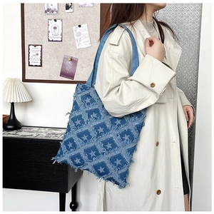 Detail of blue denim tote bag with frayed edge star patches and wide shoulder strap