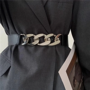 Close-up of a wide black leather belt with a chunky silver chain buckle on a grey suit