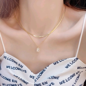 Close-up of double layer gold necklace featuring flat snake chain and gemstone pendant
