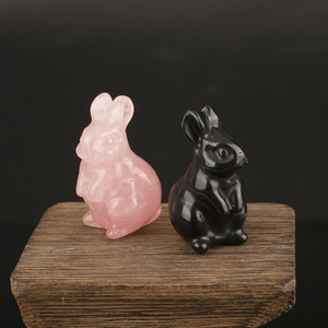 Close-up of pink and black natural crystal rabbit carvings on a dark wood base