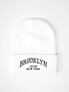 Close-up of white ribbed knit beanie featuring black Brooklyn 1898 embroidery on cuff