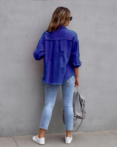 Detail view of the distressed back design with frayed hem on blue denim jacket
