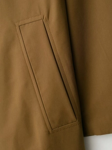 Detail of a brown trench coat showing the side pocket with diagonal weave fabric and stitching