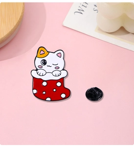 Detail of a cute white cat in a red polka dot Christmas stocking enamel pin on pink background