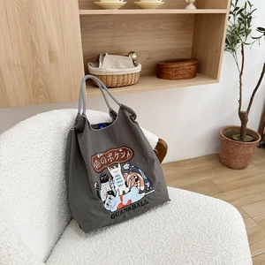 Detail of dark grey tote bag with cat illustrations on a cozy white texture chair
