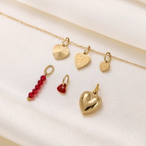 Detailed view of gold heart pendants and red beaded charms on soft white silk background