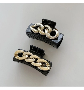 Detail of black hair claws featuring gold chain decoration and glossy finish texture