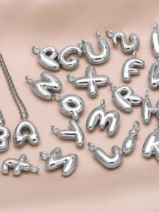 Macro shot of silver letter pendants on pink satin showing polished metal textures