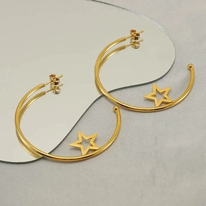 Close-up of gold C-shaped hoop earrings with hollow star charms on a mirror