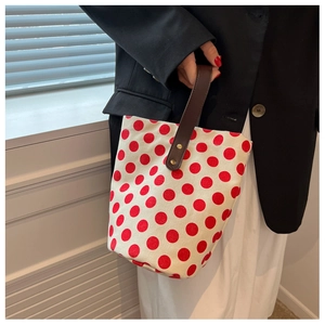 Detailed shot of a polka dot canvas bucket bag with brown leather handle held by a model