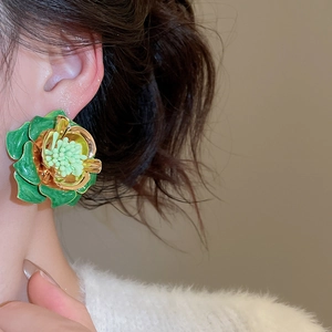 Gros plan sur les boucles d'oreilles fleurs en émail vert foncé portées à l'oreille