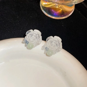 Detailed view of translucent resin flower earrings with green beads on a white porcelain dish