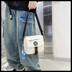 Detail of white nylon messenger bag with Pinbo logo and blue astronaut keychain
