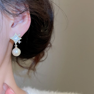 Gros plan sur boucle d'oreille étoile dorée avec perle blanche et détails en zircon