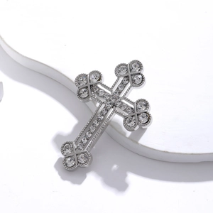 Silver cross brooch with sparkling crystals and clover ends on a white stand