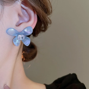 Dettaglio di un orecchino a farfalla in acrilico azzurro con zircone su una modella