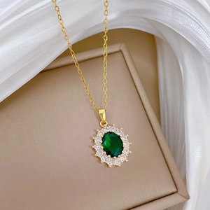 Detail of an oval green emerald pendant with crystal halo on a golden titanium steel chain