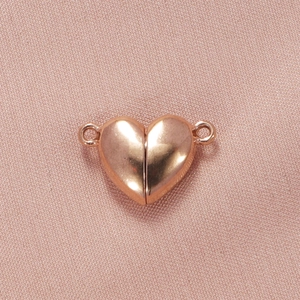 Macro shot of rose gold heart magnetic clasps for bracelets on pink fabric