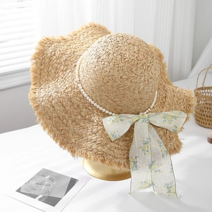 Dettaglio del cappello di paglia estivo con fiocco floreale e catena di perle