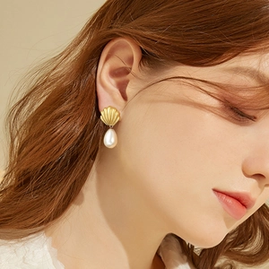 Detailed close-up of vintage gold shell earrings with waterdrop pearls worn by a model