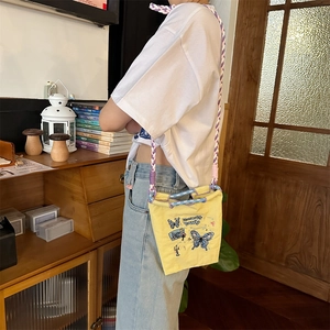 Détail du sac bandoulière en toile jaune avec broderie papillon et bandoulière tissée