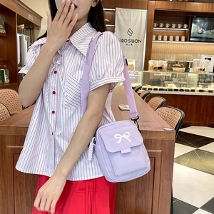 Purple crossbody bag with white bow detail and wide strap shown in a lifestyle scene