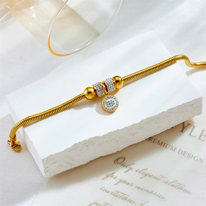 Gold snake chain bracelet with sparkling rhinestone beads and disk pendant on stone base