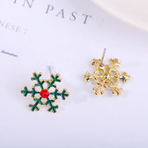 Macro view of gold-plated snowflake stud earrings with green enamel and red crystal detail