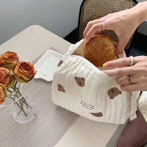 Close-up of white quilted baby bag featuring cute brown bear embroidery and zip closure