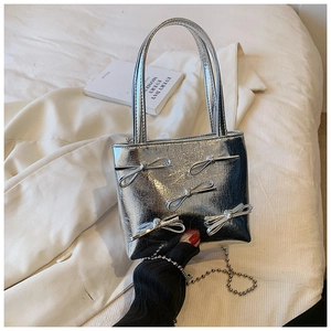Detail of silver metallic handbag with 3D bows and silver beaded chain on soft white bedding