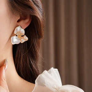 Close-up of elegant white and champagne floral stud earrings worn by a model