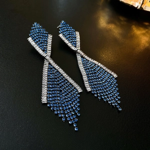 Detailed close-up of luxury tassel earrings with blue and white crystals on black leather