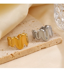 Detailed close-up of wavy 18K gold and silver plated stainless steel rings on stone