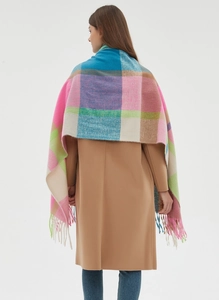 Detail view of thick rainbow plaid scarf with long tassels draped over a beige winter coat