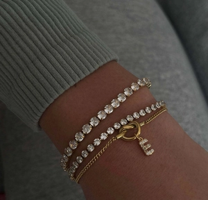 Detailed look of stacked gold letter E charm bracelet with tennis chain on wrist