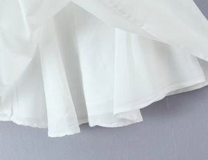 Detailed close-up showing the fine stitching and fabric texture of the white dress hemline
