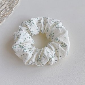 Detail of white fabric scrunchie with green floral pattern and soft pleated texture