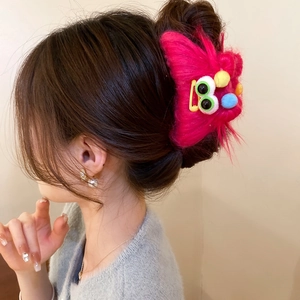 Close-up of a pink plush monster hair claw with colorful pom-poms on a model hair style