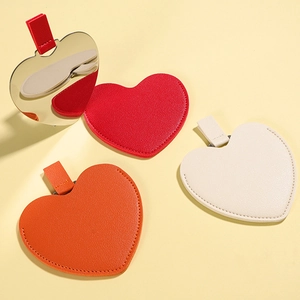 Irregular heart-shaped portable makeup mirrors in red, orange, and beige leather cases