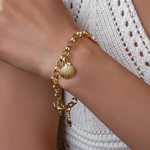 Gros plan sur un bracelet doré avec des breloques étoile de mer et coquillage sur le poignet