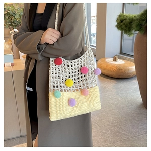 Detailed view of knitted tote bag with colorful pom-poms and beige crochet pattern