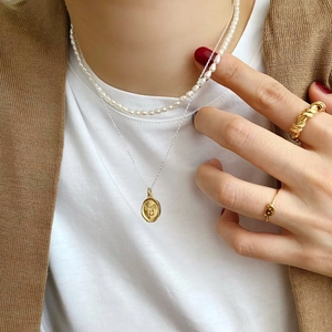 Close-up of layered gold smiley pendant necklace, pearl chain and textured woven ring set