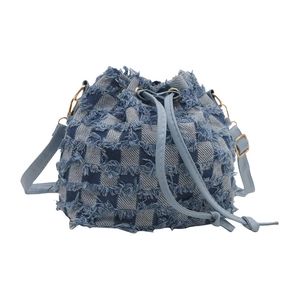 Denim drawstring bucket bag with frayed plaid texture and long shoulder strap on white base