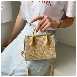 Close-up of straw woven handbag with pink floral embroidery and natural texture