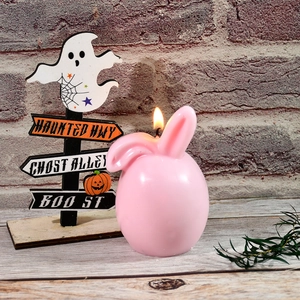 Pink bunny ear egg candle lit on a wooden table with a vintage brick wall background