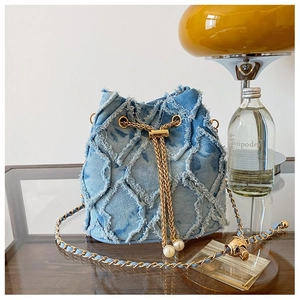 Detail of blue denim bucket bag featuring distressed edges, gold chain, and pearl charm