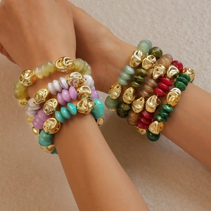 Detail of layered acrylic beaded bracelets with gold irregular metal charms on a model wrist